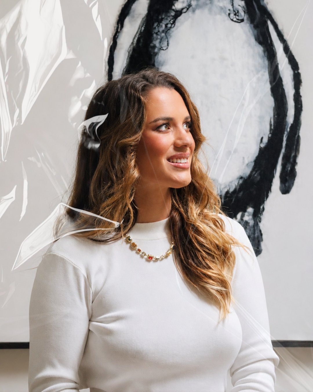 Tilly Whitfeld in a white knit, smiling in front of an ink-brush artwork